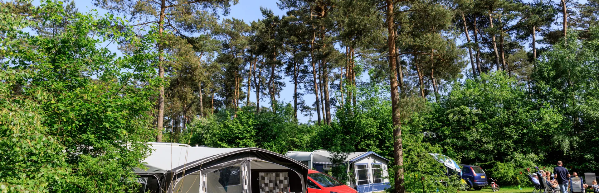 Familie ontspant bij hun caravan op een comfortplaats tussen de bomen van Ardoer Camping Diana Heide.