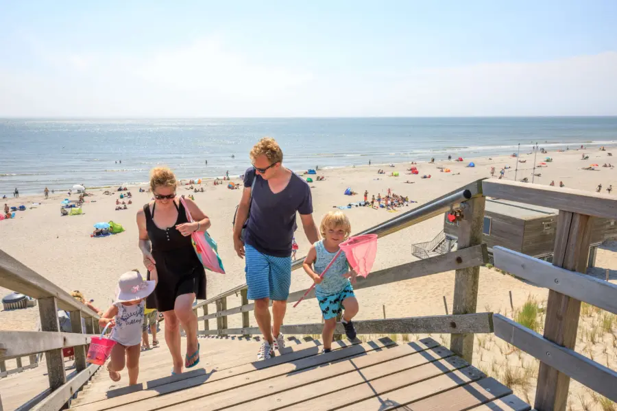 Gezin met jonge kinderen die lopen op houten trap met strand en zee op de achtergrond omgeving camping in Zeeland - Duinoord