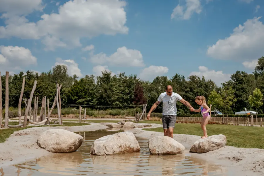 Vader helpt zijn dochter over de stapstenen in de waterspeelspeeltuin van Camping 't Geuldal.