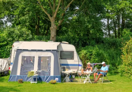Ruime kampeerplaats met caravan en voortent op camping Ginsterveld in Zeeland