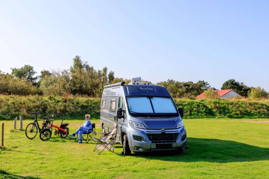 Vrouw zit buiten haar camper en er staan fietsen naast - Noorder Sandt